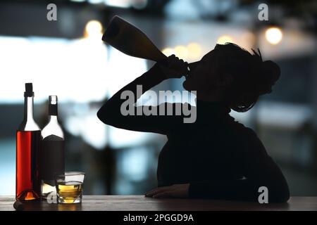 Dépendance à l'alcool. Silhouette de femme qui boit du vin mousseux dans une bouteille au bar Banque D'Images