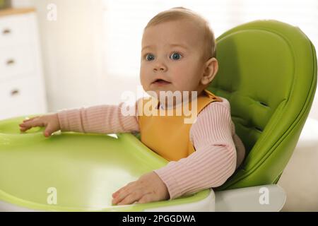 Joli petit bébé portant un bavoir dans une chaise haute à l'intérieur Banque D'Images