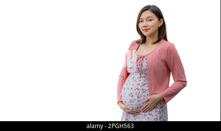 Jeune femme asiatique heureuse, vêtue de vêtements de maternité souriant et debout devant un fond blanc tenant fièrement son ventre, chambre pour copier spa Banque D'Images