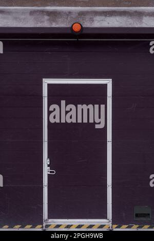 Porte de garage industrielle avec porte de passage et voyant d'alerte rouge en hiver. Banque D'Images
