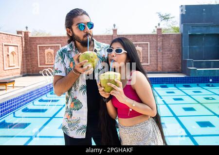 Jeune heureux couple de touristes indiens portant des lunettes de soleil boire de l'eau de noix de coco dans la chaude journée ensoleillée en plein air, vacances d'été et de vacances. Banque D'Images