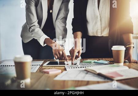 Mettre leurs plans en mouvement. Gros plan de deux femmes d'affaires utilisant une tablette numérique tout en passant par la paperasse dans un bureau. Banque D'Images