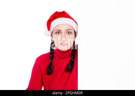 Femme surprise à Santa Hat derrière le panneau publicitaire vierge panneau isolé sur un fond blanc. Concept de vente. Banque D'Images