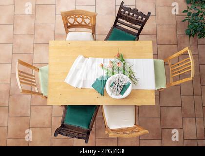 Préparation pour le dîner avec table de chemin de table, assiettes blanches, couverts, serviettes vertes et quelques fleurs de tulipe, six chaises en bois différentes, carrelage en terre cuite f Banque D'Images