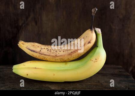 Une banane jaune mûre reposant sur une banane brune sur un fond en bois rustique Banque D'Images