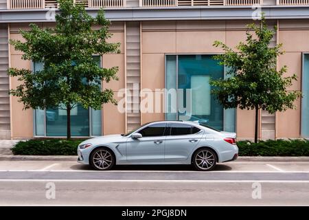 Une élégante voiture argentée se trouve en face d'un immeuble de bureaux moderne, doté de portes vitrées et d'une entrée Banque D'Images