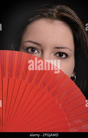 une jeune femme attirante coquetant avec un fan rouge, portrait Banque D'Images