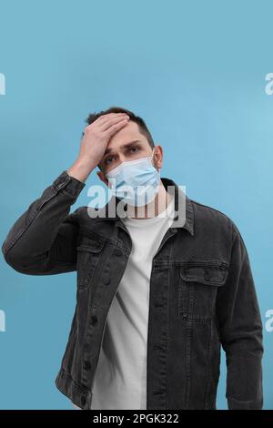 Homme en masque souffrant de maux de tête sur fond bleu clair. Symptômes du rhume Banque D'Images