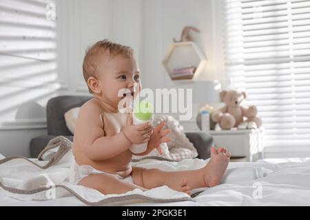 Adorable petit bébé avec bouteille de poudre à dépoussiérer sur le lit à la maison, espace pour le texte Banque D'Images