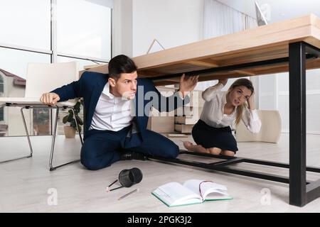 Les employés ont peur de se cacher sous le bureau pendant le tremblement de terre Banque D'Images