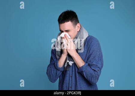 Jeune homme soufflant le nez dans le tissu sur fond bleu. Symptômes du rhume Banque D'Images