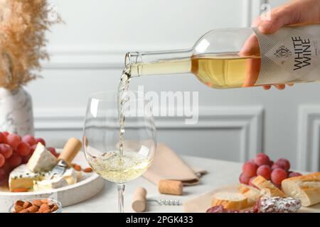 Femme versant du vin blanc de la bouteille dans le verre à la table avec des en-cas, gros plan Banque D'Images