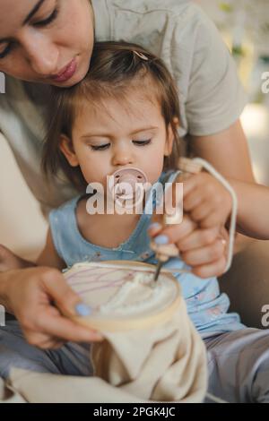 Gros plan portrait mère et petite fille tricoter ensemble, assis sur le sol, tenant des aiguilles. Profitez de votre temps libre et de votre créativité Banque D'Images