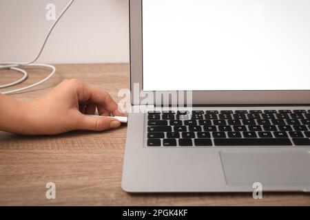 Femme connectant le câble de charge à l'ordinateur portable sur une table en bois, en gros plan. Espace pour le texte Banque D'Images