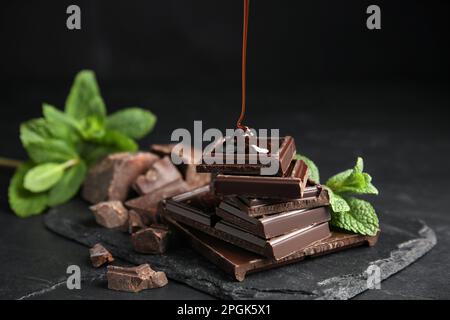 Verser le sirop sur les morceaux de chocolat et la menthe sur la table noire, fermer Banque D'Images