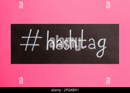 Papier noir avec mot hashtag et symbole sur fond rose, vue de dessus Banque D'Images