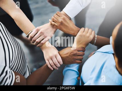 Restez à proximité de ceux qui vous motivent continuellement. Photo en grand angle d'un groupe d'hommes d'affaires tenant un poignet d'un autre dans une formation circulaire. Banque D'Images