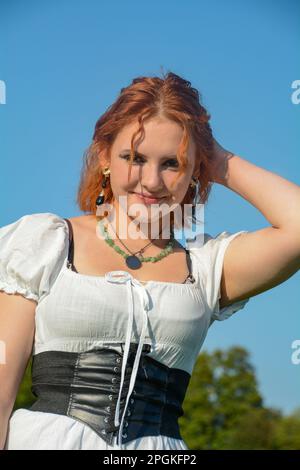 Portrait d'une jolie jeune femme portant un dessus blanc, debout à l'extérieur sous un ciel bleu Banque D'Images