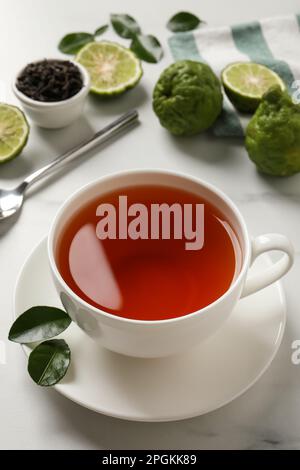 Tasse de délicieux thé bergamote et fruits frais sur table blanche Banque D'Images