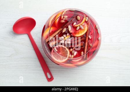 Bol en verre de délicieux punch aromatique et louche sur table en bois blanc, plat Banque D'Images