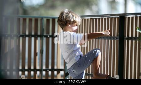 Enfant tenant dans une clôture en bois de balcon dans le bâtiment résidentiel de l'appartement. Concept de sécurité et de protection du petit garçon en terrasse Banque D'Images