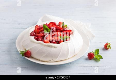 Gâteau classique Pavlova meringue à la crème fouettée et aux fraises, arrosé de sucre en poudre sur fond bleu clair, sélectif Banque D'Images