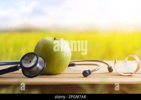 Concept de santé et de contrôle avec pomme et stéthoscope et mètre ruban autour sur table en bois avec fond de nature. Vue avant. Banque D'Images