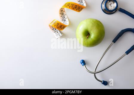 Pomme, stéthoscope et mètre ruban sur table blanche représentant la santé, la nutrition et le contrôle du corps. Vue de dessus. Banque D'Images