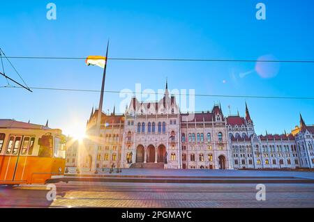 Le coucher de soleil lumineux derrière le Parlement gothique très orné sur la place Lajos Kossuth avec le tramway jaune en premier plan, Budapest, Hongrie Banque D'Images