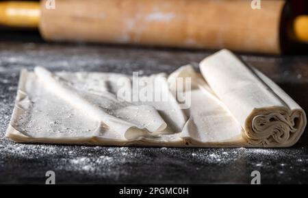 Pâte phyllo et rouleau en bois, gros plan sur une face sombre. Banque D'Images