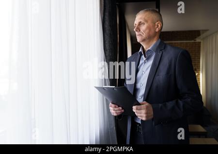 Portrait d'un homme d'affaires qui tient des documents entre ses mains, regarde par la fenêtre. Banque D'Images