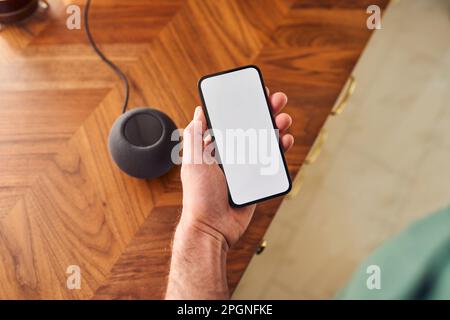 Homme connectant un téléphone avec écran vierge à une enceinte intelligente sur le comptoir de la cuisine Banque D'Images