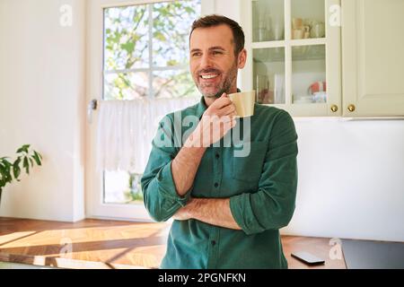 Homme mûr debout dans la cuisine buvant du café Banque D'Images