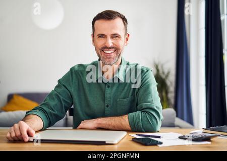 Homme assis au bureau avec un ordinateur portable qui travaille à la maison Banque D'Images