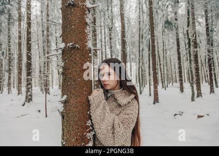 Jeune fille contemplative debout près d'un arbre dans une forêt enneigée Banque D'Images