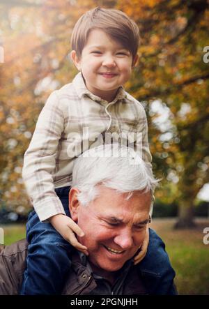 Garçon souriant assis sur l'épaule du grand-père au parc Banque D'Images