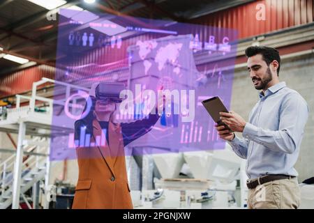 Femme d'affaires portant des lunettes VR avec un collègue utilisant une tablette PC en usine Banque D'Images