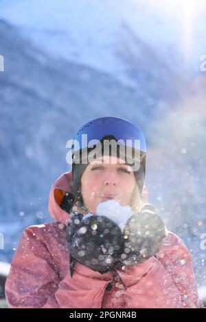 Femme souriante portant des gants soufflant sur la neige Banque D'Images