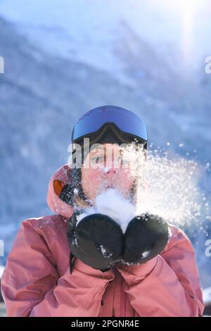 Femme portant des gants soufflant sur la neige Banque D'Images