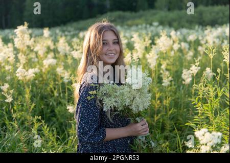 Jeune femme souriante tenant un bouquet de fleurs debout dans le champ Banque D'Images