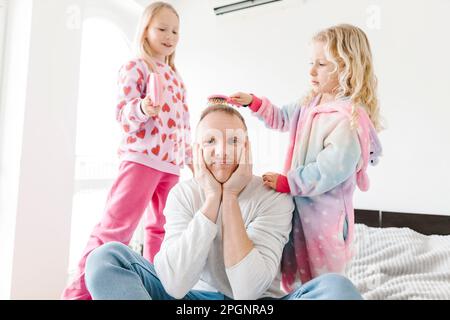 Les filles se brossent les cheveux d'un père assis sur le lit à la maison Banque D'Images