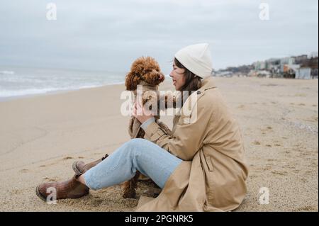 Femme appréciant avec un chien de compagnie assis à la plage Banque D'Images