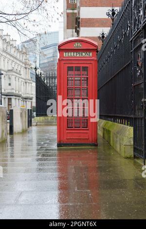 Téléphone traditionnel rouge dans une rue humide de Londres avec une résection sur une chaussée mouillée Banque D'Images