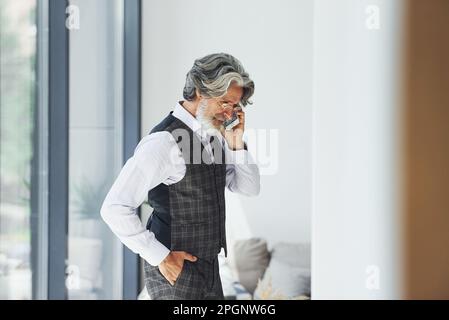 Un homme d'affaires prospère utilise le téléphone. Homme moderne et élégant avec cheveux gris et barbe à l'intérieur Banque D'Images