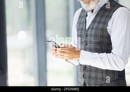 Un homme d'affaires prospère utilise le téléphone. Homme moderne et élégant avec cheveux gris et barbe à l'intérieur Banque D'Images