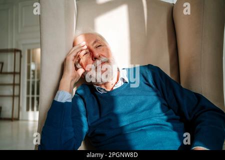 Homme senior contemplatif assis sur un fauteuil à la maison Banque D'Images