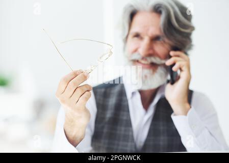 Un homme d'affaires prospère utilise le téléphone. Homme moderne et élégant avec cheveux gris et barbe à l'intérieur Banque D'Images