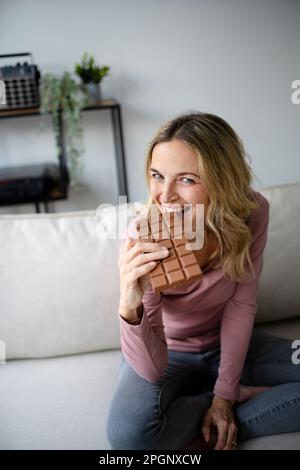 Bonne femme mangeant du chocolat sur le canapé à la maison Banque D'Images