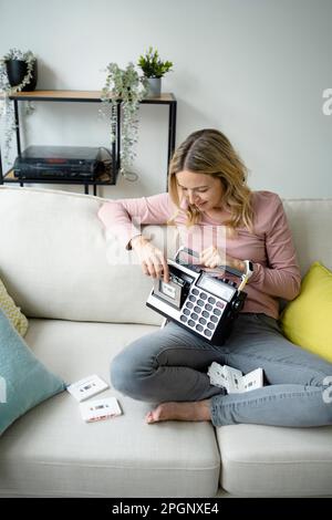 Femme mûre souriante avec lecteur de cassettes assis sur un canapé à la maison Banque D'Images