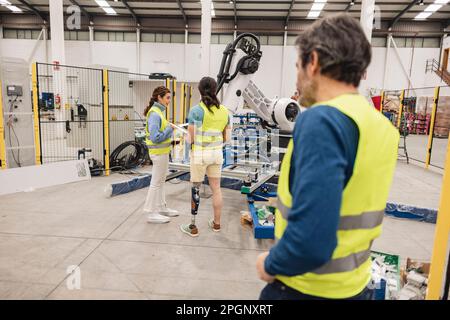 Les ingénieurs portant des vêtements réfléchissants dans une usine de robotique Banque D'Images